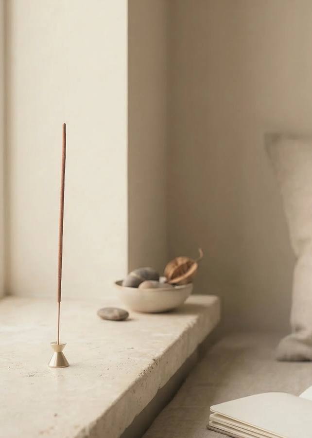 Single incense stick burning in a minimalist brass holder