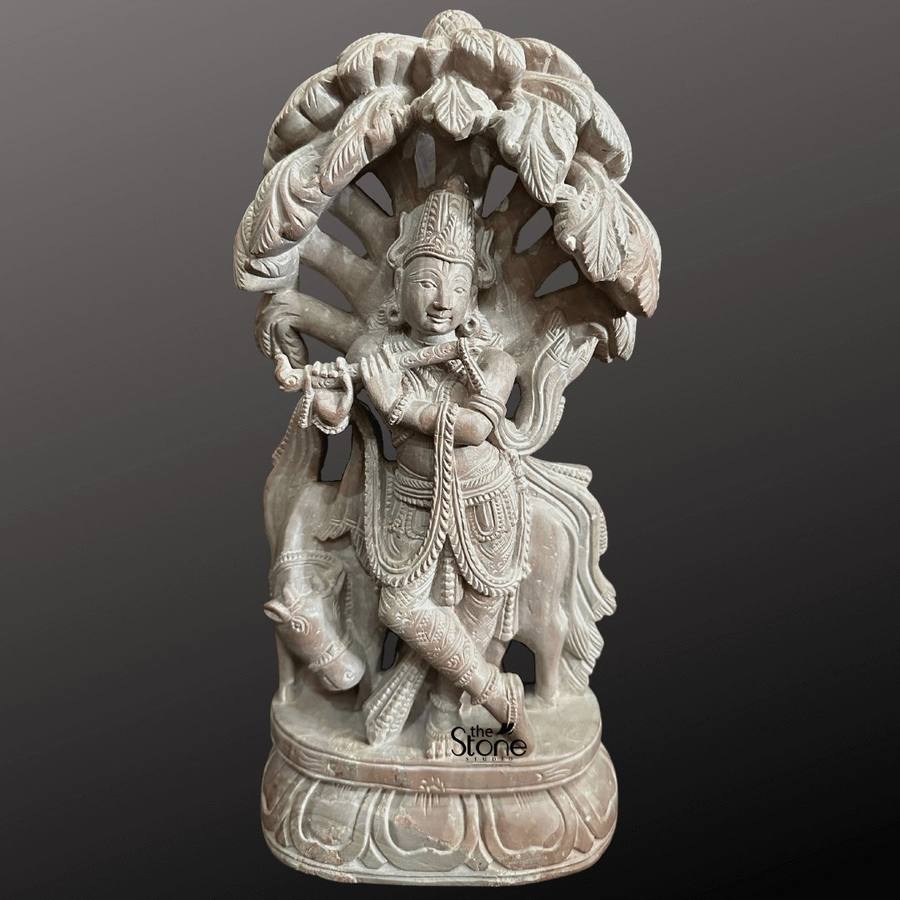 Carved stone idol of Krishna with cow under a tree